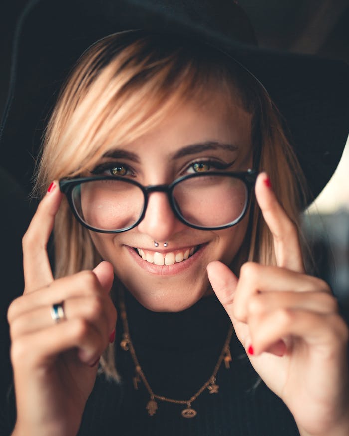 Close-up portrait of a smiling woman wearing glasses and a black hat, showcasing a modern hipster style.
