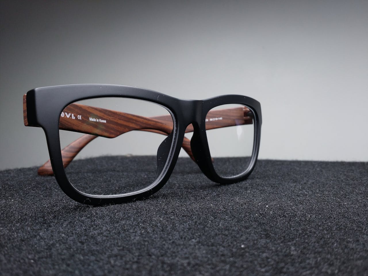 Close-up of fashionable black and wooden frame glasses on dark fabric with a soft-focus background.